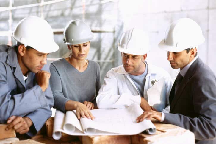 project engineer in a meeting with other project engineers standing around reading a piping and instrument diagram.